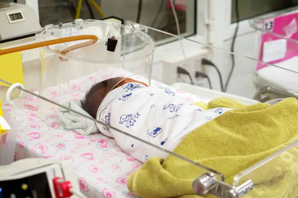 A sick newborn with respiratory problems sleeping on the baby bed and wear the oxygen box for helps to breathe more easily and cure of Respiratory in the hospital.
