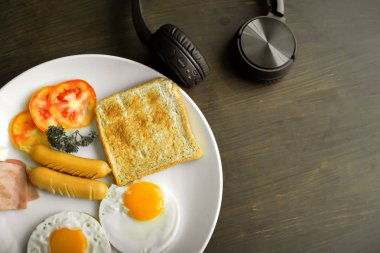 Koyu kahverengi ahşap masa üzerinde Amerikan kahvaltı ve siyah kulaklık Üstten Görünüm.