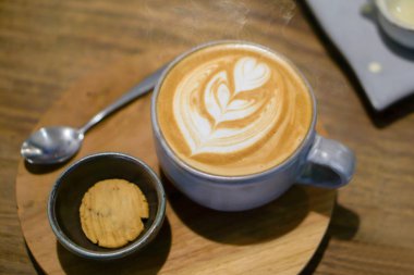 Top görünümünde geç kahve ve geç sanat siyah seramik kase ahşap plaka üzerinde bir çerezde ve kafedeki masa mavi seramik kahve fincanı.