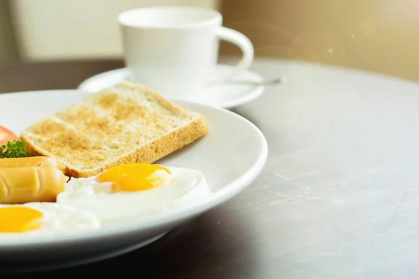 American breakfast and hot coffee in a white ceramic coffee cup on a wooden table with warm morning sunshine and lens flare background.