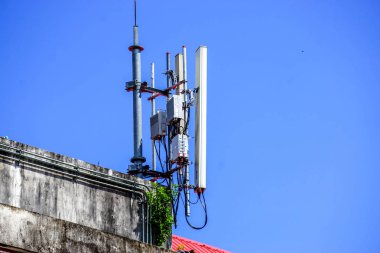 Devices and Receivers Communication Signal with antennas on the top of building and bright blue sky background. clipart