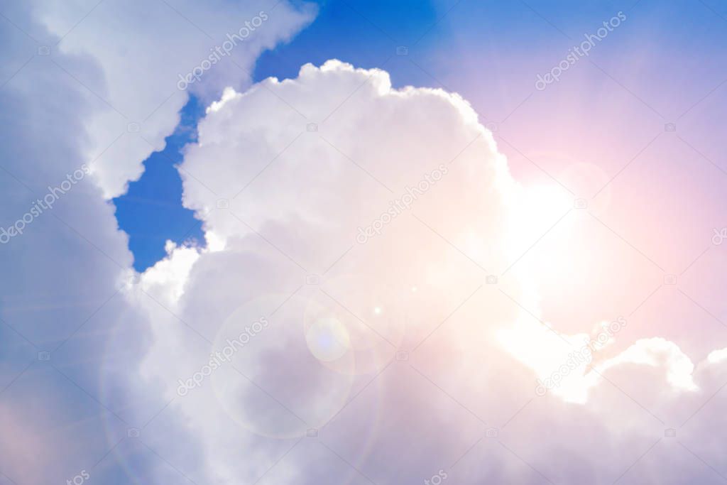 Big white cloud with sun and lens flare on bright blue sky.