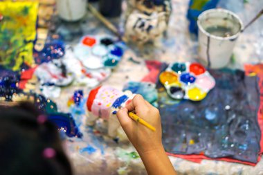 Resim fırçası eğitimi alan ve sanat sınıfındaki ahşap oyuncak bebek üzerinde boya öğrenen öğrencilerin yakın çekim elleri..