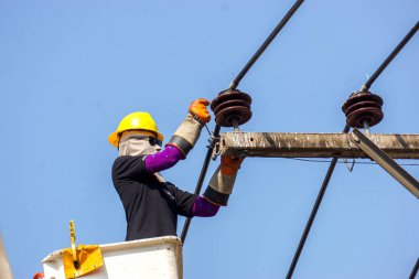 Yakın plan elektrikçiler açık mavi gökyüzü arkaplanı altında elektrik hattını onarmak için teleferik üzerinde çalışıyorlar.