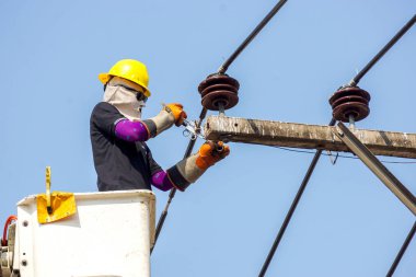 Yakın plan elektrikçiler açık mavi gökyüzü arkaplanı altında elektrik hattını onarmak için teleferik üzerinde çalışıyorlar.