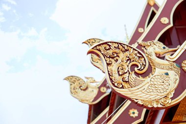 Çok güzel bir altın ve ahşap oyması Tayland tapınağının çatısında kuş şeklinde eski bir desen ve parlak mavi gökyüzü arkaplanı..