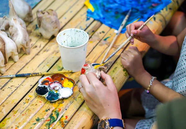 Closeup hands of art students holding paint brush study and learning paint on wood animal doll in the art classroom.