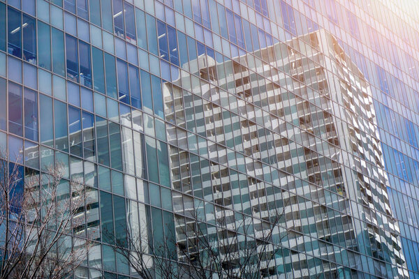 Osaka, Japan-January 18, 2019 : Closeup and crop reflection of buildings and bright blue sky on glass office building windows with sun flare.