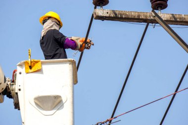 Yakın plan elektrikçiler açık mavi gökyüzü arkaplanı altında elektrik hattını onarmak için teleferik üzerinde çalışıyorlar.