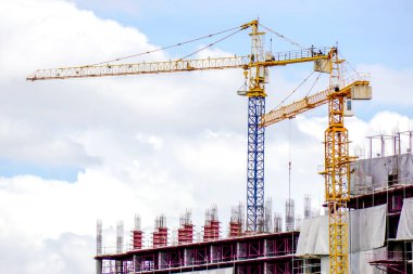 Çekici vinçler açık mavi gökyüzü ve büyük bulut arkaplanı üzerinde bina inşaatında çalışıyor.
