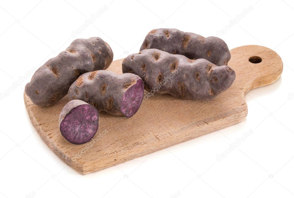 Vitelotte, purple potato in piles on a wooden cutting board