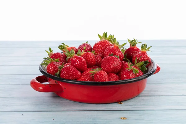 Strawberries in an old red enamelled dish on a blue background