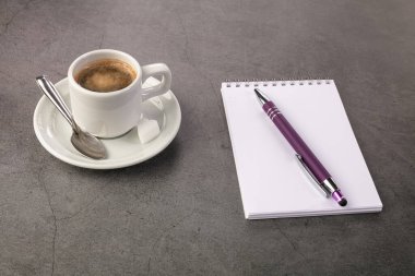 Kahve fincanı, telefon ve arka planda bir defter.