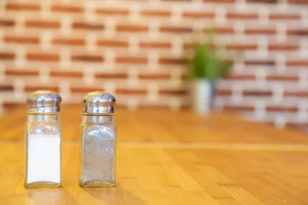 Pepper shaker and salt shaker on a bamboo table with a brick background