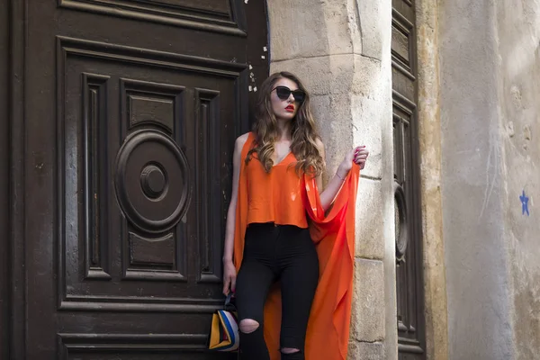 Estilo de vida retrato de uma jovem mulher elegante vestindo calças pretas, top laranja e um saco de mão listrado — Fotografia de Stock