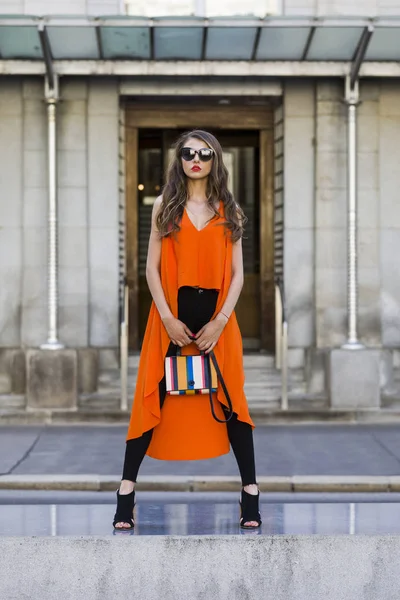 Estilo de vida retrato de uma jovem mulher elegante vestindo calças pretas, top laranja e um saco de mão listrado — Fotografia de Stock
