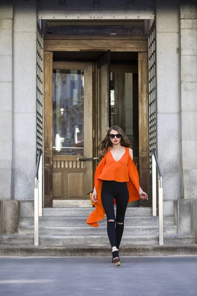 Estilo de vida retrato de uma jovem mulher elegante vestindo calças pretas, top laranja e um saco de mão listrado — Fotografia de Stock