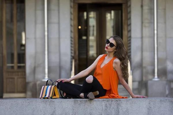 Estilo de vida retrato de uma jovem mulher elegante vestindo calças pretas, top laranja e um saco de mão listrado — Fotografia de Stock