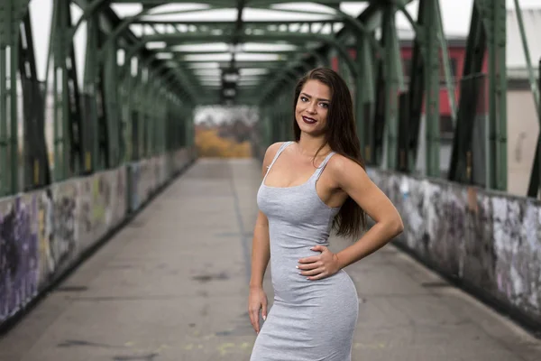 Jovem morena vestindo vestido cinza e de pé em uma ponte com graffiti — Fotografia de Stock