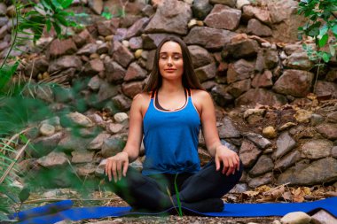 Genç bir kadın parkta yoga yapıyor ve eğitiyor. Açık hava kadınlarının sporu