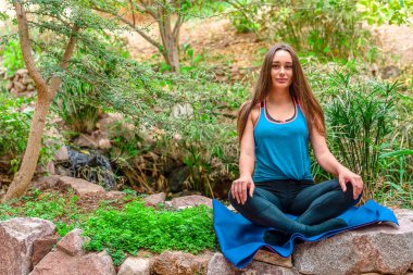 Genç bir kadın parkta yoga yapıyor ve eğitiyor. Açık hava kadınlarının sporu