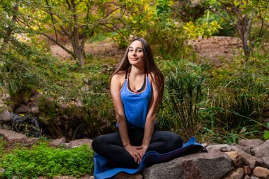 Genç bir kadın parkta yoga yapıyor ve eğitiyor. Açık hava kadınlarının sporu