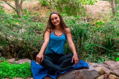 Genç bir kadın parkta yoga yapıyor ve eğitiyor. Açık hava kadınlarının sporu