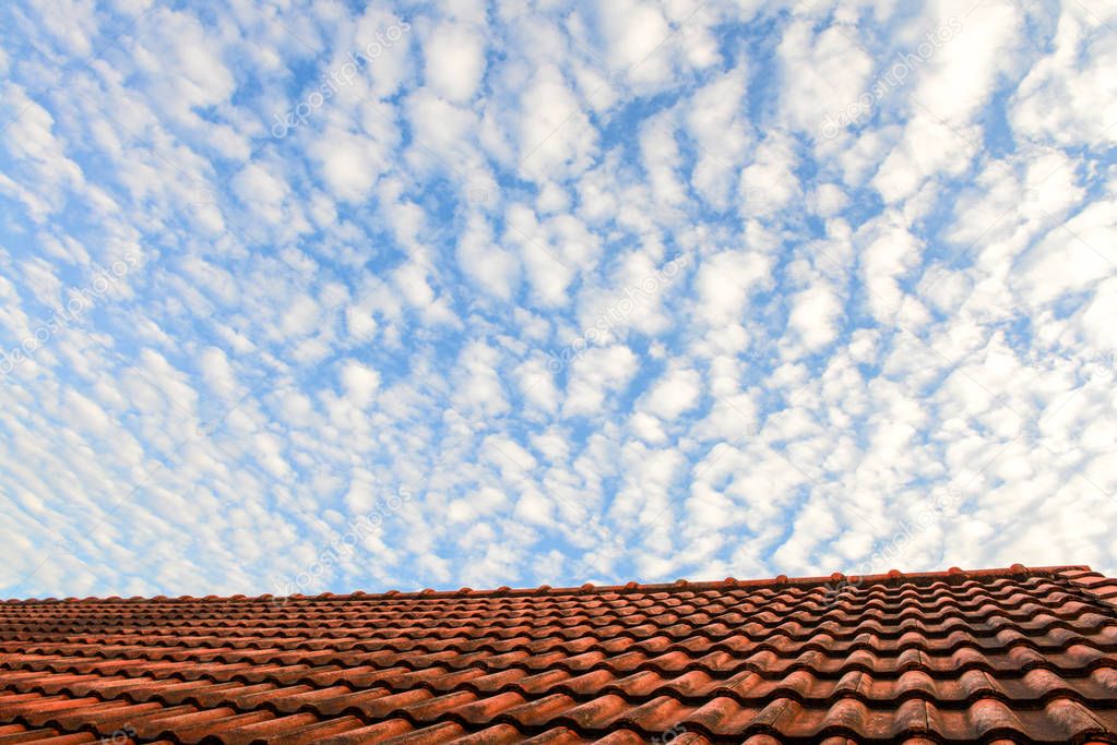 Red house roof and blue sky with white fluffy clouds