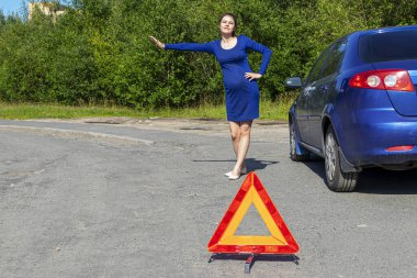 Kaputu açık kırık bir arabanın yanında el kaldırmış genç bir kadının fotoğrafı. Araba sigortası kavramı