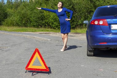 Kaputu açık kırık bir arabanın yanında el kaldırmış genç bir kadının fotoğrafı. Araba sigortası kavramı