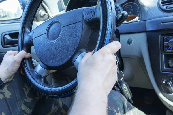 Hands on steering wheel of a car driving on an asphalt blurred road