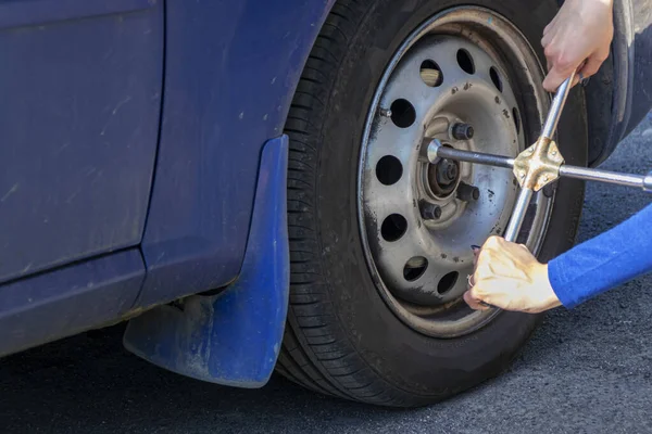 Bella ragazza con la chiave del cilindro cambia la ruota nella macchina rotta. Pneumatici di ricambio sul lato della strada di campagna. Concetto assicurazione auto — Foto Stock