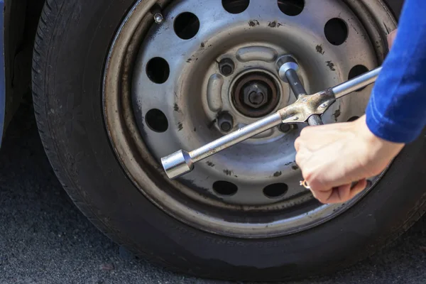 Piękna dziewczyna z kluczem cylindra zmienia koło w zepsutym samochodzie. Wymiana opon na poboczu drogi krajowej. Koncepcja ubezpieczenia samochodu — Zdjęcie stockowe