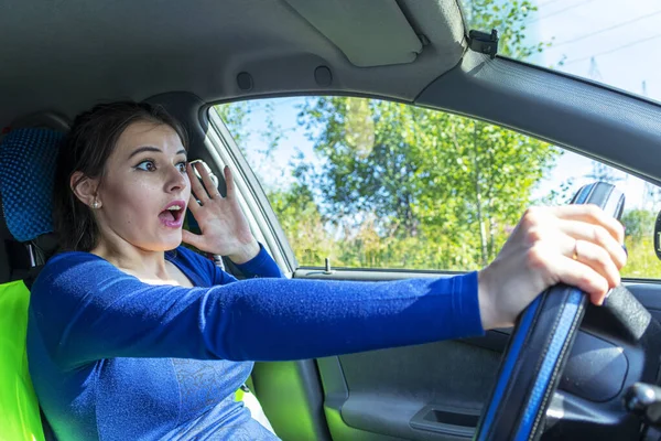 Angry woman driving a car. The girl with an expression of displeasure is actively gesticulating behind the wheel of the car. Car insurance concept — Stock Photo, Image