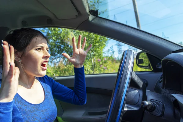 Una donna arrabbiata che guida un'auto. La ragazza con un'espressione di dispiacere sta gesticolando attivamente al volante dell'auto. Concetto assicurazione auto — Foto Stock