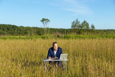 Sakallı, beyaz, beyaz, beyaz bir adam dışarıda bir laptopta çalışıyor. Kavramsal iş adamı açık havada.