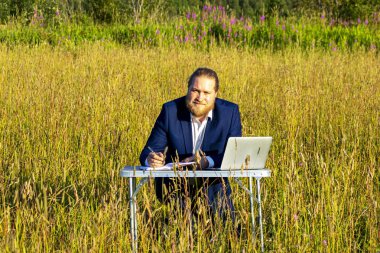 Sakallı, beyaz, beyaz, beyaz bir adam dışarıda bir laptopta çalışıyor. Kavramsal iş adamı açık havada.