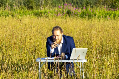 Sakallı, beyaz, beyaz, beyaz bir adam dışarıda bir laptopta çalışıyor. Kavramsal iş adamı açık havada.