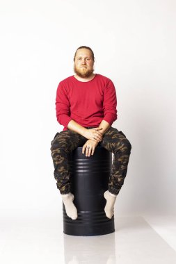 Beyaz arka planda siyah bir fıçı taşıyan kırmızı kazaklı beyaz bir adam.