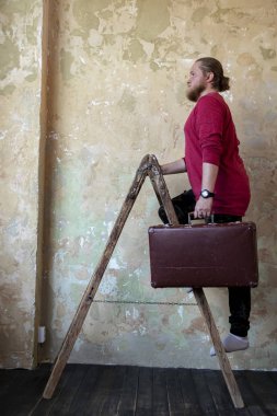 Merdivende kırmızı ceketli, sakallı, beyaz bir adam.