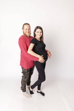 Kırmızı kazaklı, sakallı beyaz bir adam hamile, beyaz bir kıza sarılıyor.