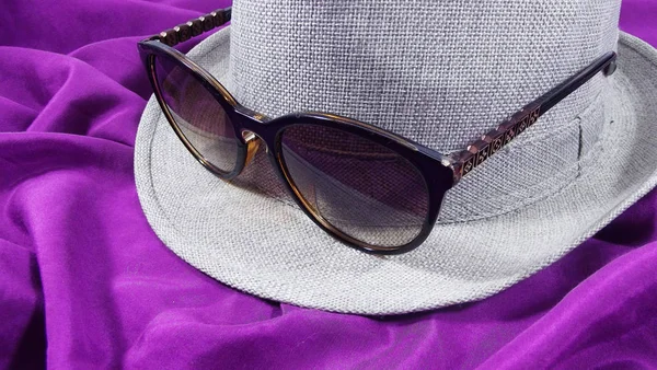 Women's hat and glasses on a purple background.