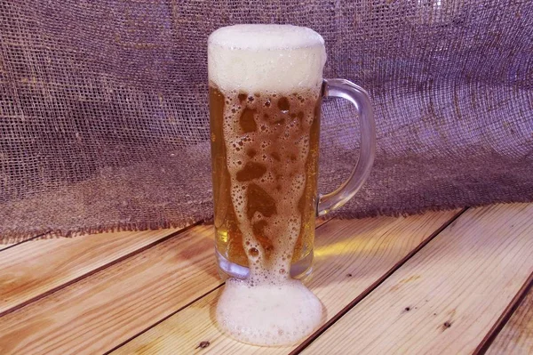 Mug of fresh beer on wood and burlap background.