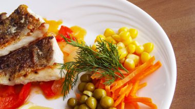 Kızarmış Balık beyaz bir tabakta sebze ile.