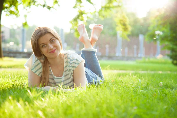 Usměvavá mladá žena leží na trávě — Stock fotografie