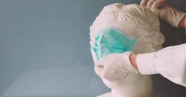 Руки, надевающие медицинскую маску на гипсовую голову Венеры — стоковое видео