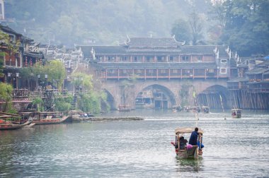 Çin 'in Hunan Eyaleti' ndeki Fenghuang antik sahil kasabasında Tuojiang Rover boyunca ilerleyen bir turist botu Gökkuşağı köprüsüne doğru ilerliyor.