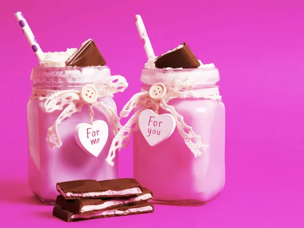 Two tasty strawberry pink cocktail with ice cream with whipped cream and chocolate in a beautiful jar with a heart on a pink background. There are slices of chocolate nearby. — Stock Photo, Image