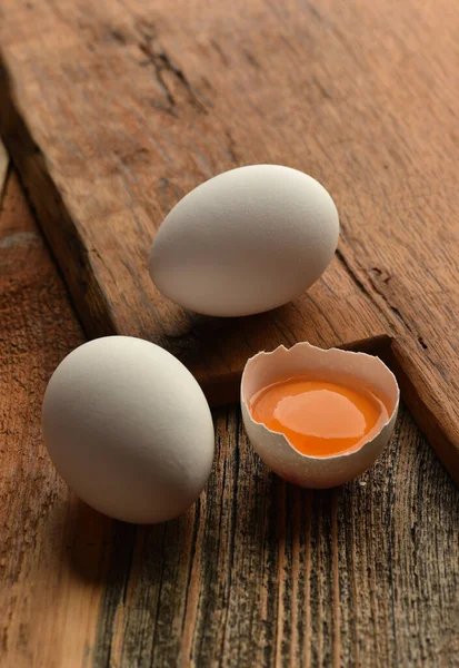 Chicken eggs and half broken egg with yolk on wooden background