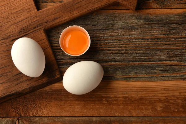 Chicken eggs and half broken egg with yolk on wooden background